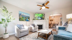 A living room with a fireplace, two sofas, a coffee table, and a large TV mounted above the fireplace. - Walk to Broad Ripple & Monon Trail | Fire Pit | Family Home | Sleeps 8 (Indianapolis)