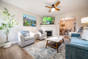 A living room with a fireplace, two sofas, a coffee table, and a large TV mounted above the fireplace.