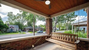 A covered porch with a wooden bench, brick walls, and a view of a residential street. - Walk to Broad Ripple & Monon Trail | Fire Pit | Family Home | Sleeps 8 (Indianapolis)