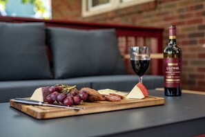 A wooden board with cheese, grapes, and sliced meats on a table, a glass of red wine, and a bottle of wine in a restaurant setting.