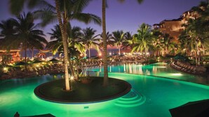A resort pool area with palm trees, lounge chairs, and a building with multiple balconies. - Luxury 1BR Suite at Villa del Palmar Flamingos – Beachfront Resort (Nay.)