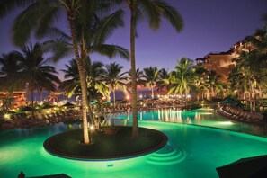 Ein Poolbereich eines Resorts mit Palmen, Liegestühlen und einem Gebäude mit mehreren Balkonen.
