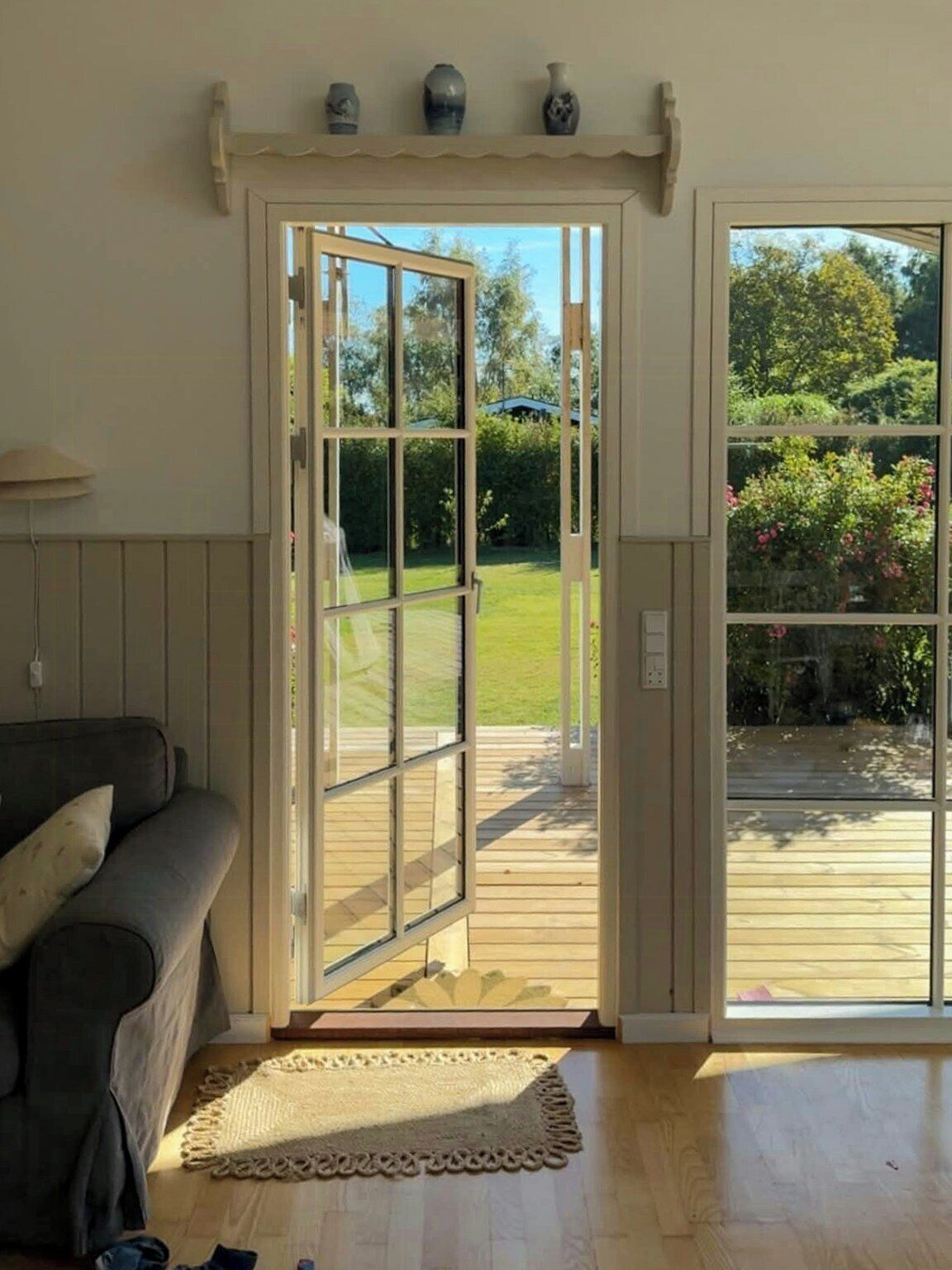 A room with a wooden floor, a grey sofa, a white rug, and a glass door leading to an outdoor deck.