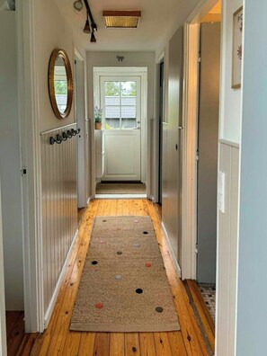 A hallway with a wooden floor, a rug with holes, a mirror, and a door leading to a window. - Summer house on Fejø with field views and beach (Fejø)