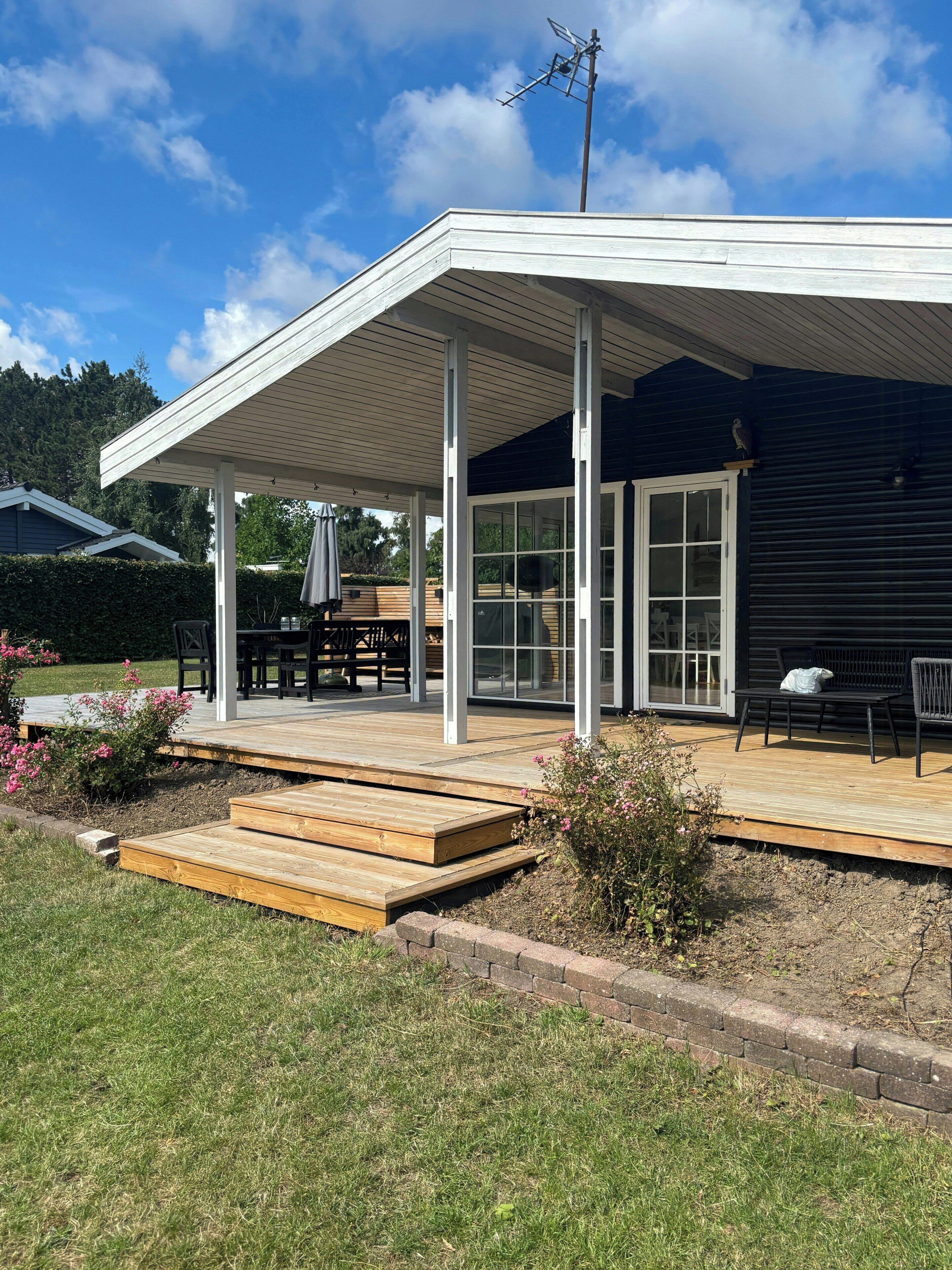 Un espacio al aire libre techado con piso de madera, una mesa, sillas y un banco.