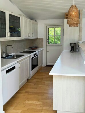 A modern kitchen with white cabinetry, a built-in oven, a sink, and a coffee maker. - Summer house on Fejø with field views and beach (Fejø)
