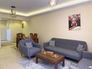A living room with a grey sofa, two armchairs, a coffee table, and a dining area with wooden chairs and a table. - CK 803 . Spacious 2BR Apt., 2 Baths (Sheikh Zayed City)