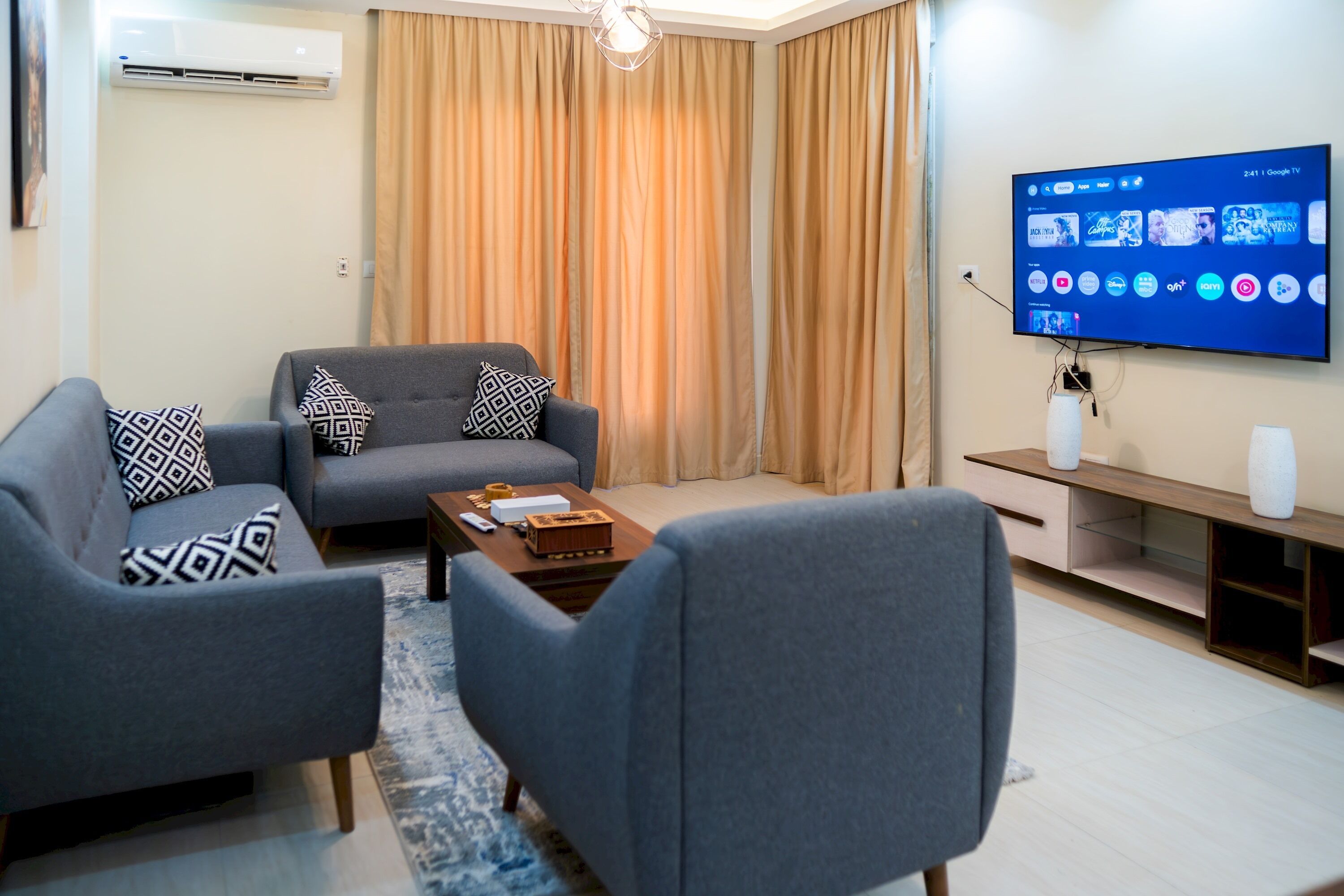 A modern living room with a grey sofa set, a coffee table, and a flat-screen TV mounted on the wall.