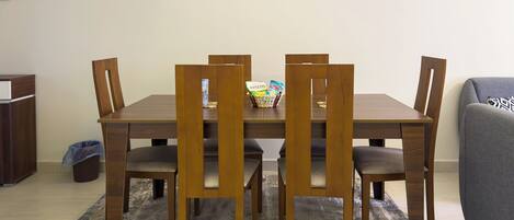 Un comedor con una mesa y sillas de madera, un cubo de basura pequeño y un sofá gris.