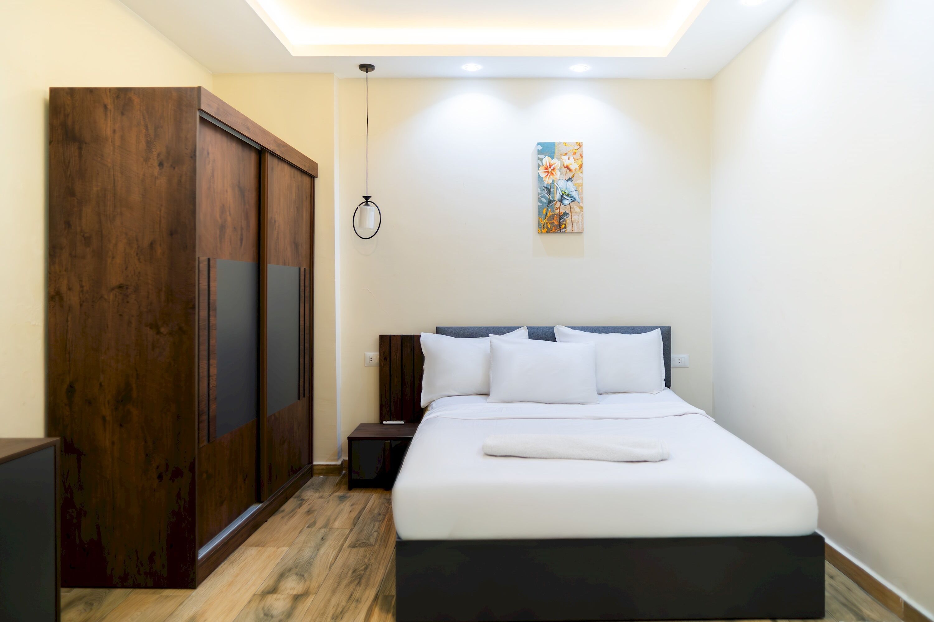 A bedroom with a bed, a wardrobe, a nightstand, and a painting on the wall.