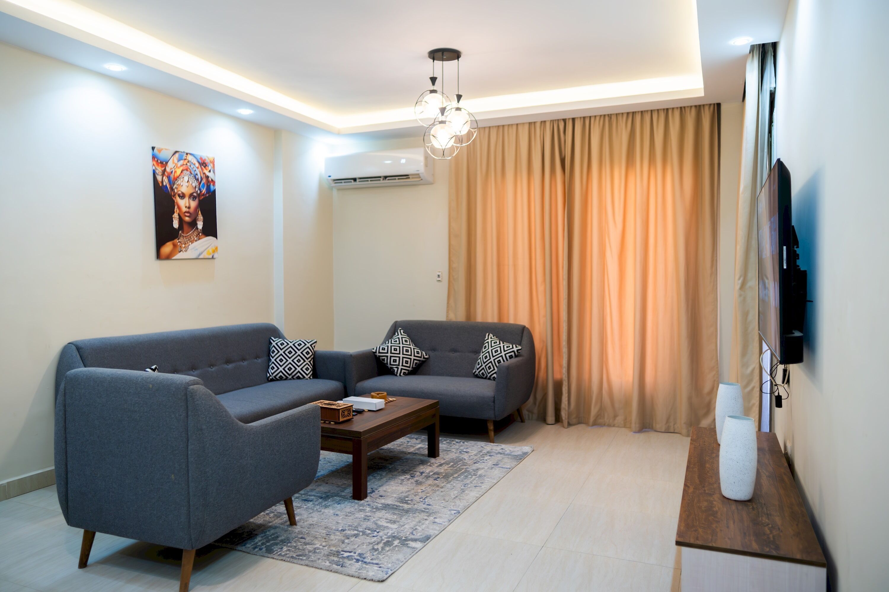 Un salon moderne avec un canapé gris, une table basse et un téléviseur à écran plat fixé au mur.