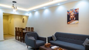A modern living room with a sofa, armchairs, a coffee table, and a dining area with chairs and a table. - CK 803 . Spacious 2BR Apt., 2 Baths (Sheikh Zayed City)