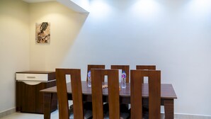 A dining area with a wooden table and chairs, a water bottle on the table, and a painting on the wall. - CK 803 . Spacious 2BR Apt., 2 Baths (Sheikh Zayed City)