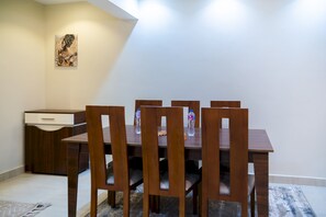 A dining area with a wooden table and chairs, a water bottle on the table, and a painting on the wall.
