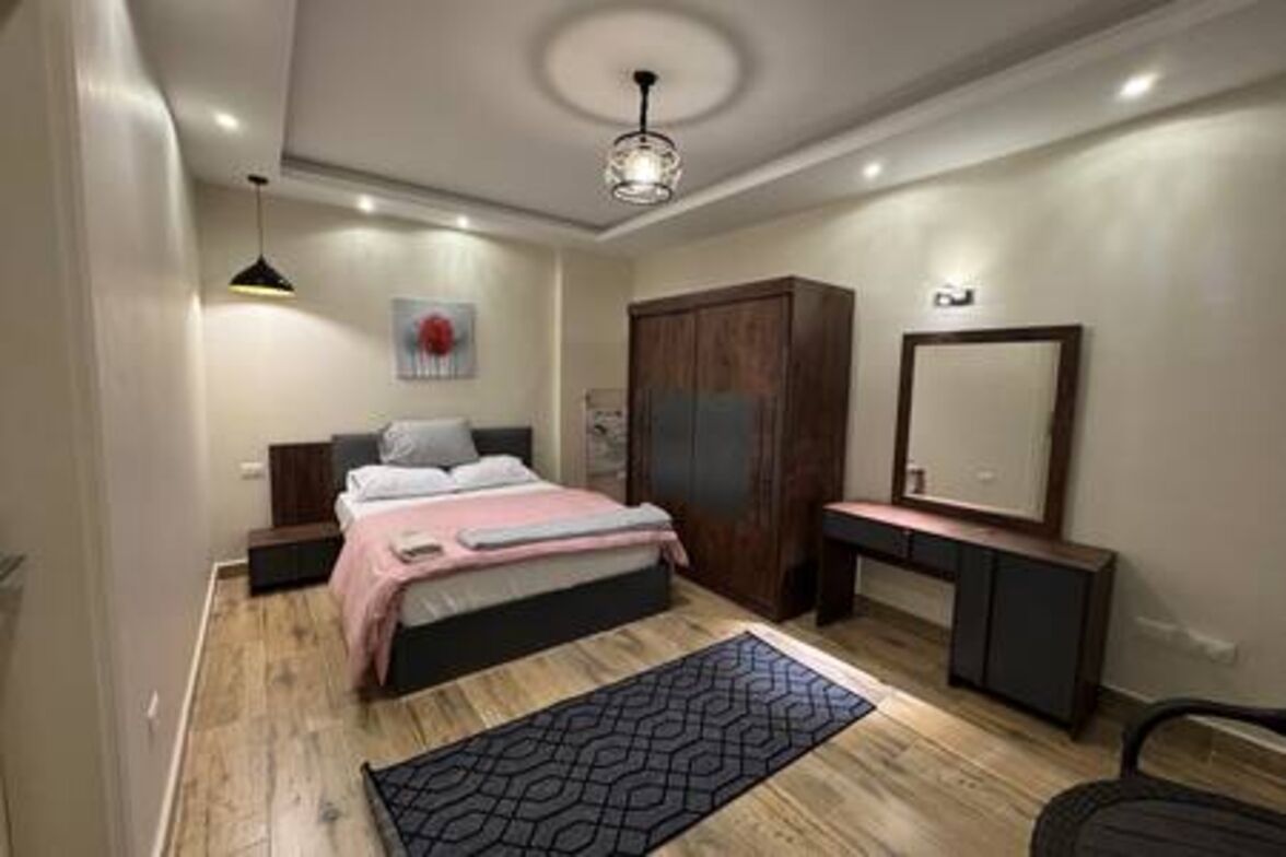 Un dormitorio con cama, mesita de noche, cómoda, espejo y lámpara de techo.