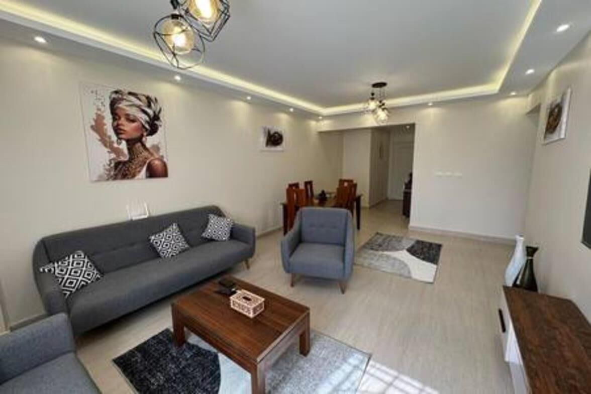A modern living room with a sofa, armchair, coffee table, and a dining area in the background.