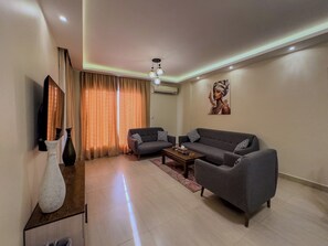 A modern living room with a grey sofa, a coffee table, and a TV. - CK 903 . Spacious 2BR Apt., 2 Baths (Sheikh Zayed City)