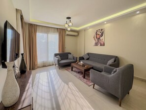Ein modernes Wohnzimmer mit einer Couch, Sesseln, einem Couchtisch und einem Fernseher.