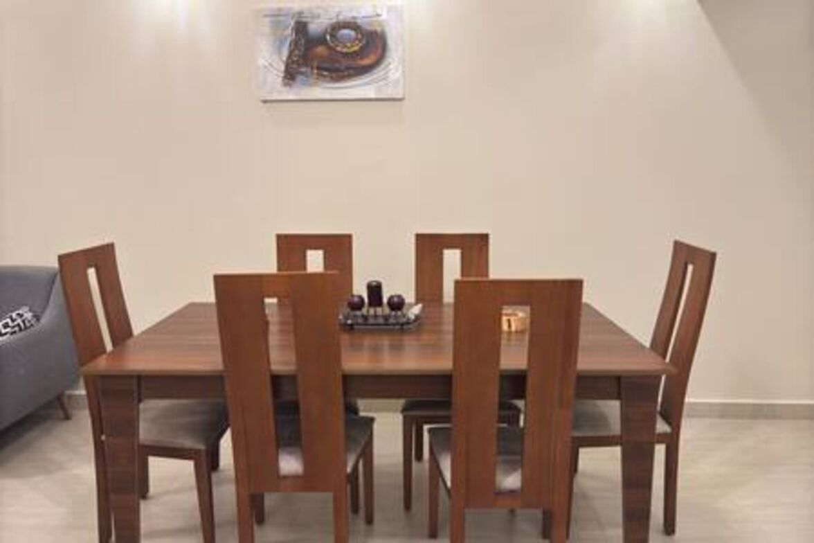 Un coin repas avec une table en bois et quatre chaises, un petit objet décoratif posé sur la table, et un canapé gris en arrière-plan.