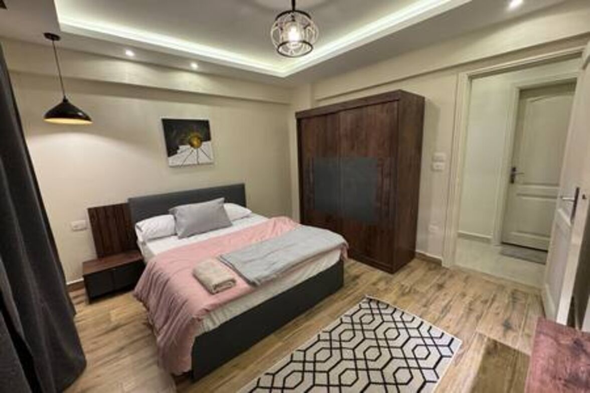 Une chambre à coucher comprenant un lit, des tables de chevet, une armoire, un tapis à motifs et un luminaire au plafond.