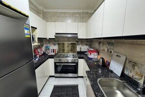 Eine kleine Küche mit weißen Schränken, einem Edelstahlkühlschrank, einem eingebauten Backofen und einer schwarzen Arbeitsplatte.