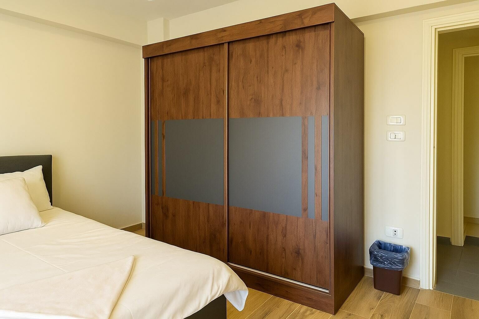 Quarto com uma cama, um guarda-roupa de madeira e uma lixeira.