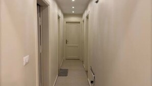 A narrow hallway with a door at the end, a light switch on the wall, and a power outlet on the right side. - CK 903 . Spacious 2BR Apt., 2 Baths (Sheikh Zayed City)