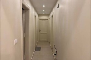 Ein schmaler Flur mit einer Tür am Ende, einem Lichtschalter an der Wand und einer Steckdose auf der rechten Seite.