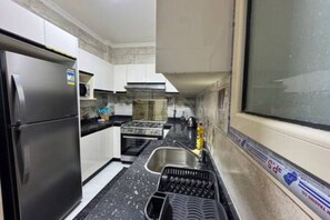 A compact kitchen with a stainless steel refrigerator, a microwave, a stove, and a sink. - CK 903 . Spacious 2BR Apt., 2 Baths (Sheikh Zayed City)