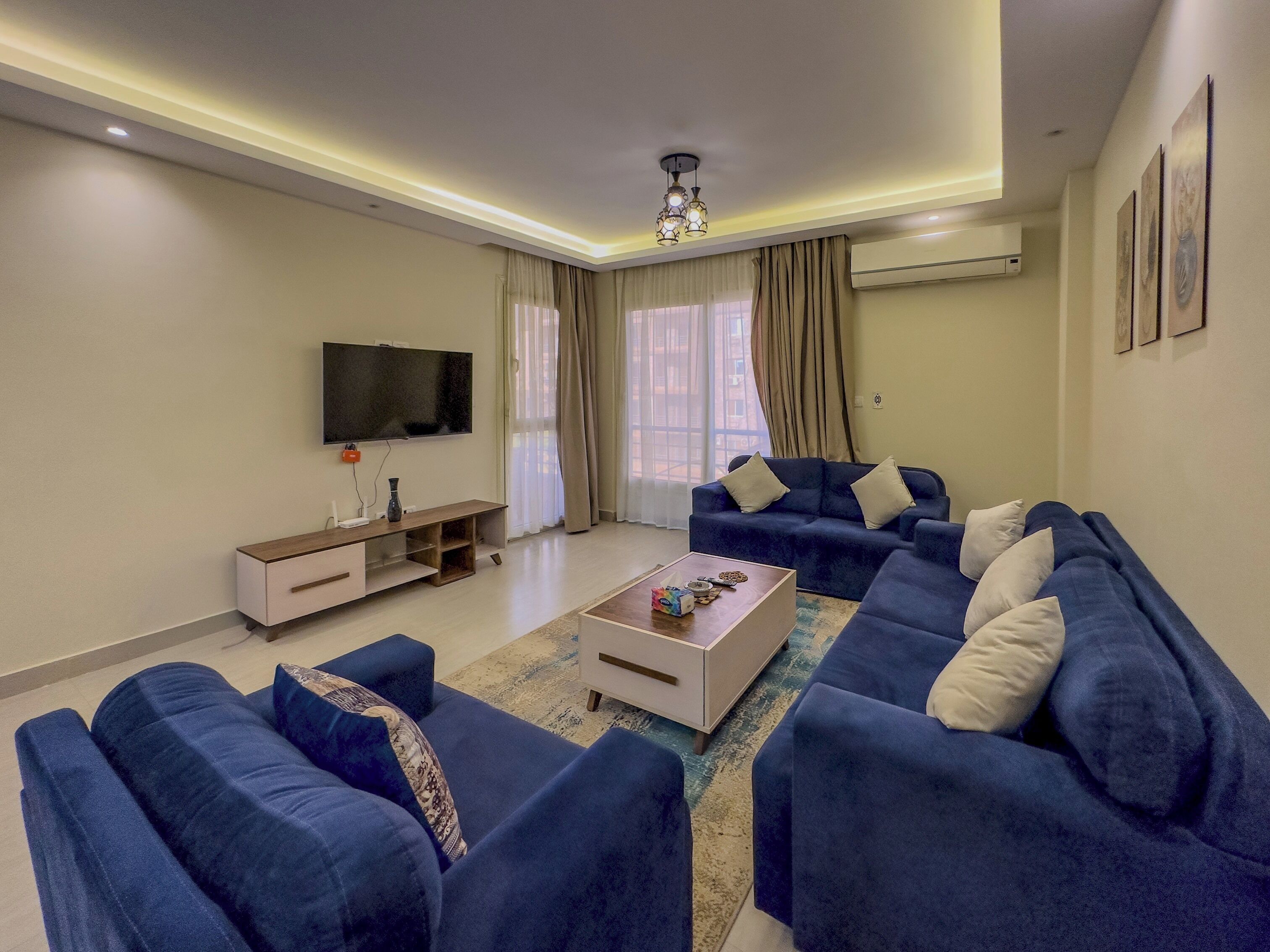 Una sala de estar moderna con un sofá modular, una mesa de centro, un televisor de pantalla plana y una lámpara de techo.