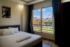 Ein Hotelzimmer mit einem Bett, einem Gemälde und Blick auf Gebäude und Grünflächen.