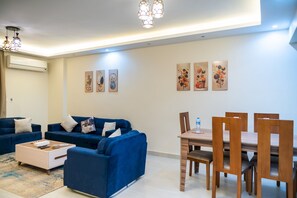 Ein modernes Wohnzimmer mit einem blauen Sofa, einem Couchtisch und einem Essbereich mit Holzsesseln und einem Tisch.