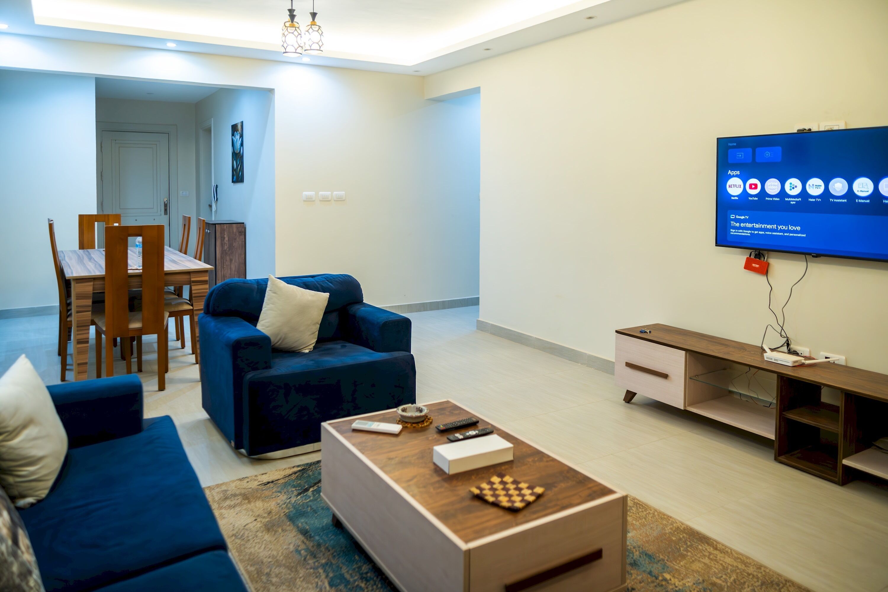 Een moderne woonkamer met een blauwe bank, een salontafel en een flatscreen televisie aan de muur.