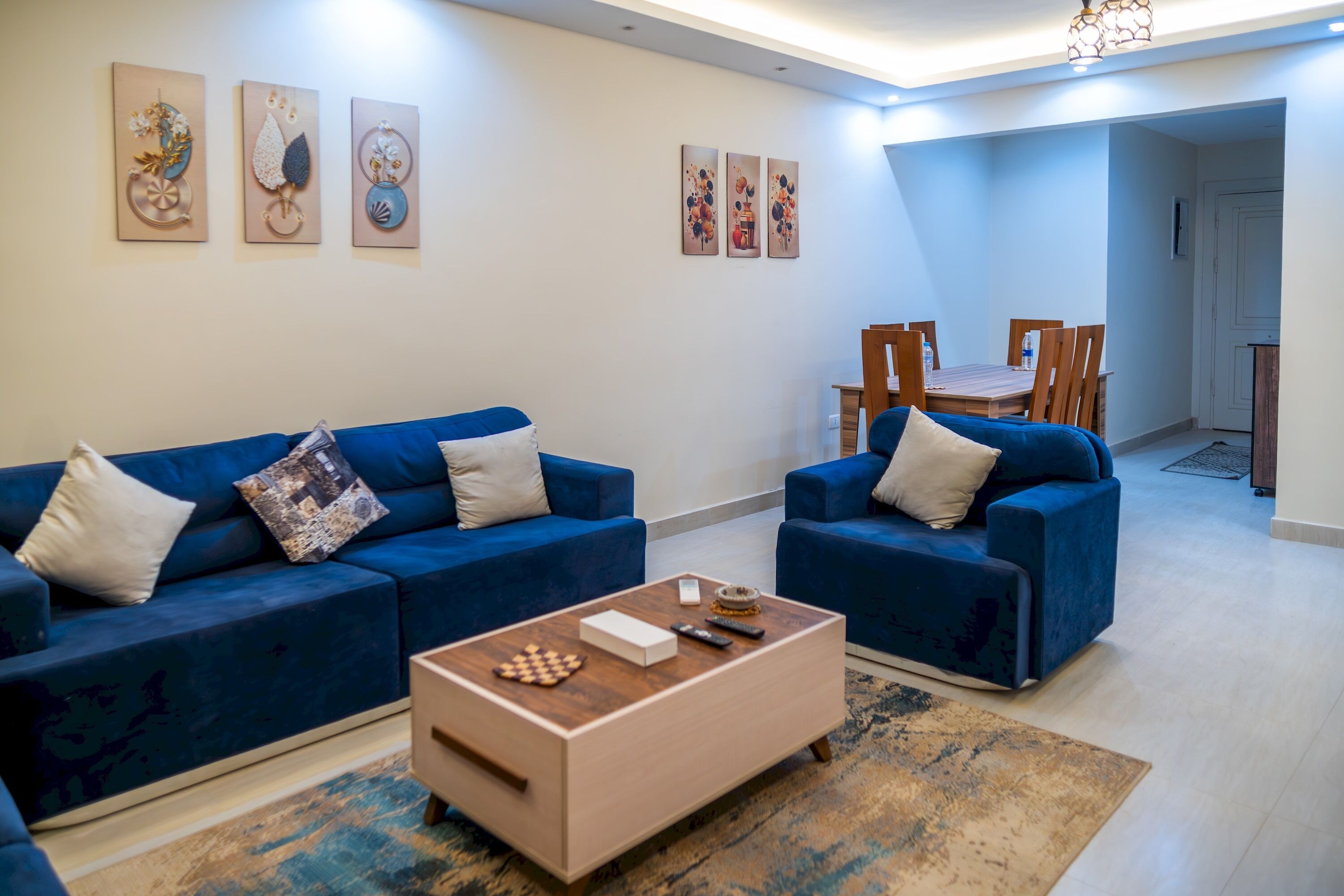 A living room with two blue sofas, a coffee table, and artwork on the walls.