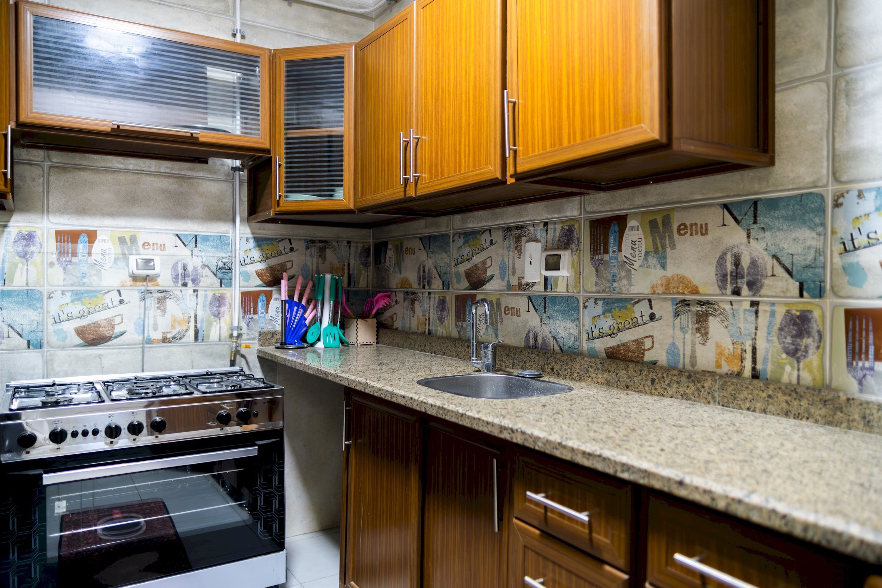 A kitchen with wooden cabinets, a gas stove, and a tiled backsplash with kitchen utensils.