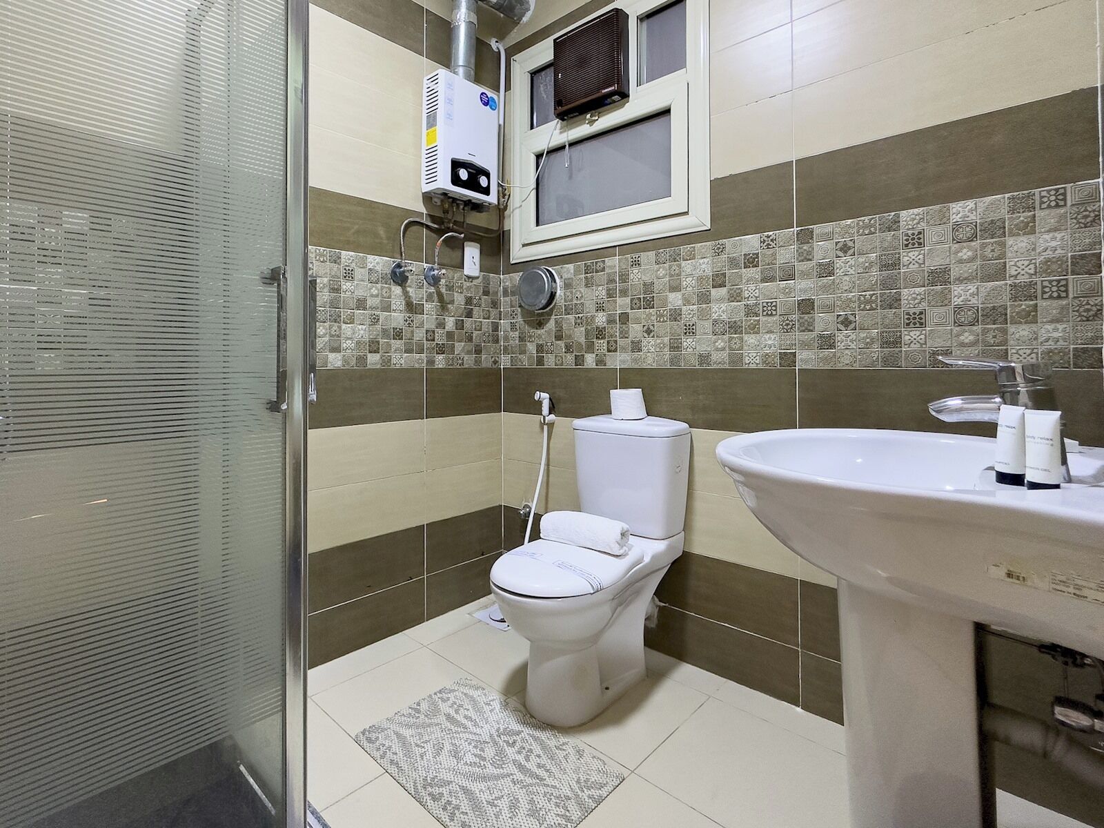 Ein Badezimmer mit Toilette, Waschbecken, Dusche und Lüftungsanlage.