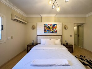A hotel room with a large bed, a ceiling fan, an air conditioning unit, a painting, and a door. - 1406.  Elegant 2BR Apt | Sun Terrace | Ensuite (Almazah)