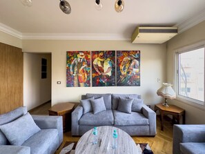 A living room with a grey sofa, a coffee table, and a painting on the wall. - 1406.  Elegant 2BR Apt | Sun Terrace | Ensuite (Almazah)