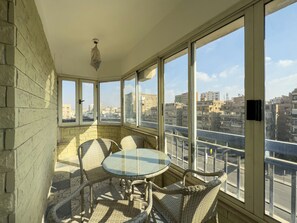 A balcony with a glass table and wicker chairs, overlooking a cityscape. - 1406.  Elegant 2BR Apt | Sun Terrace | Ensuite (Almazah)