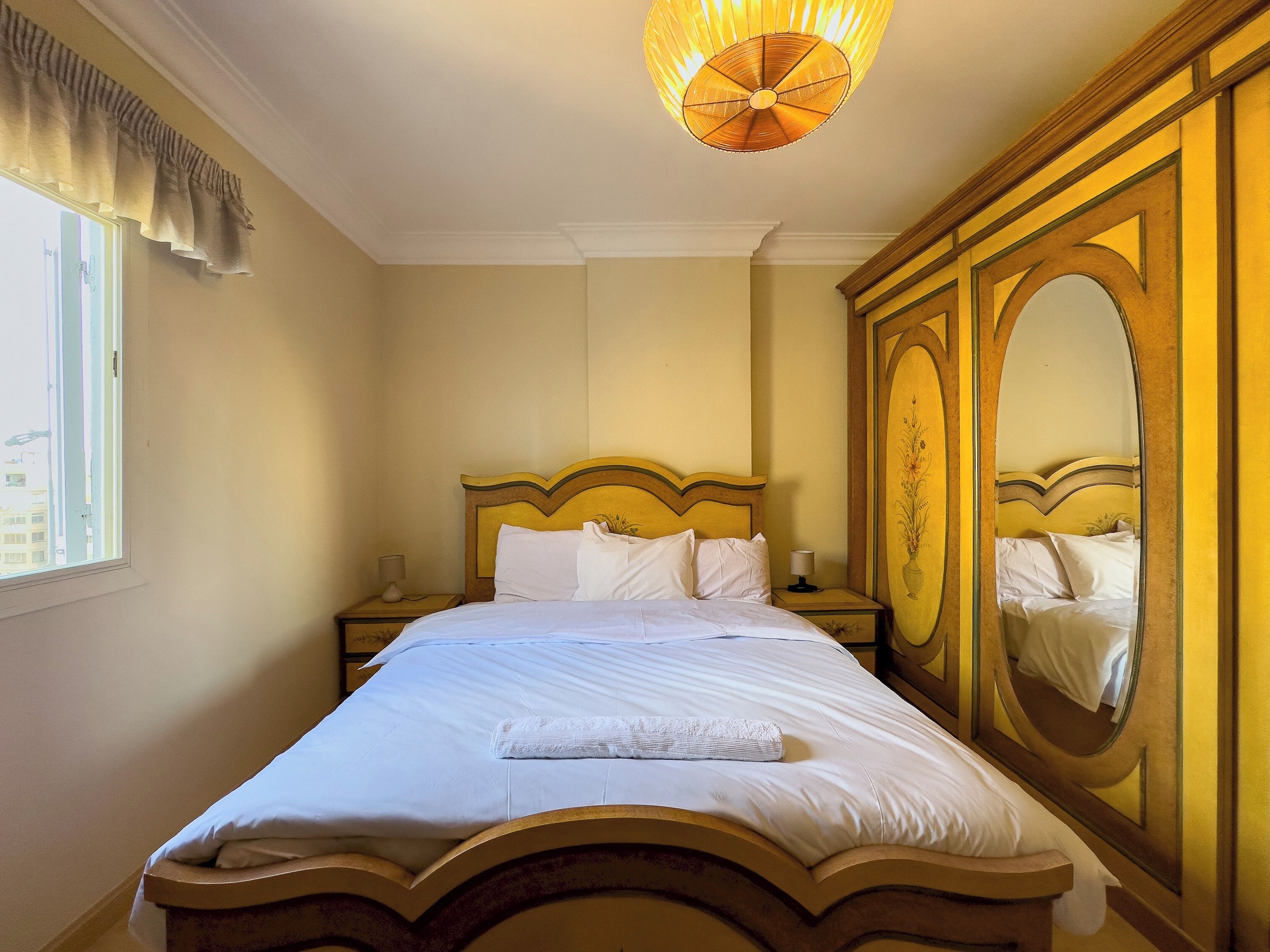 A neatly made bed with white linens, a bedside lamp, and a large mirror on the wall.