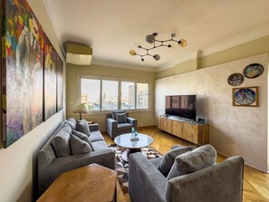 A living room with a sofa set, a coffee table, a TV on a wooden cabinet, and artwork on the walls. - 1406.  Elegant 2BR Apt | Sun Terrace | Ensuite (Almazah)