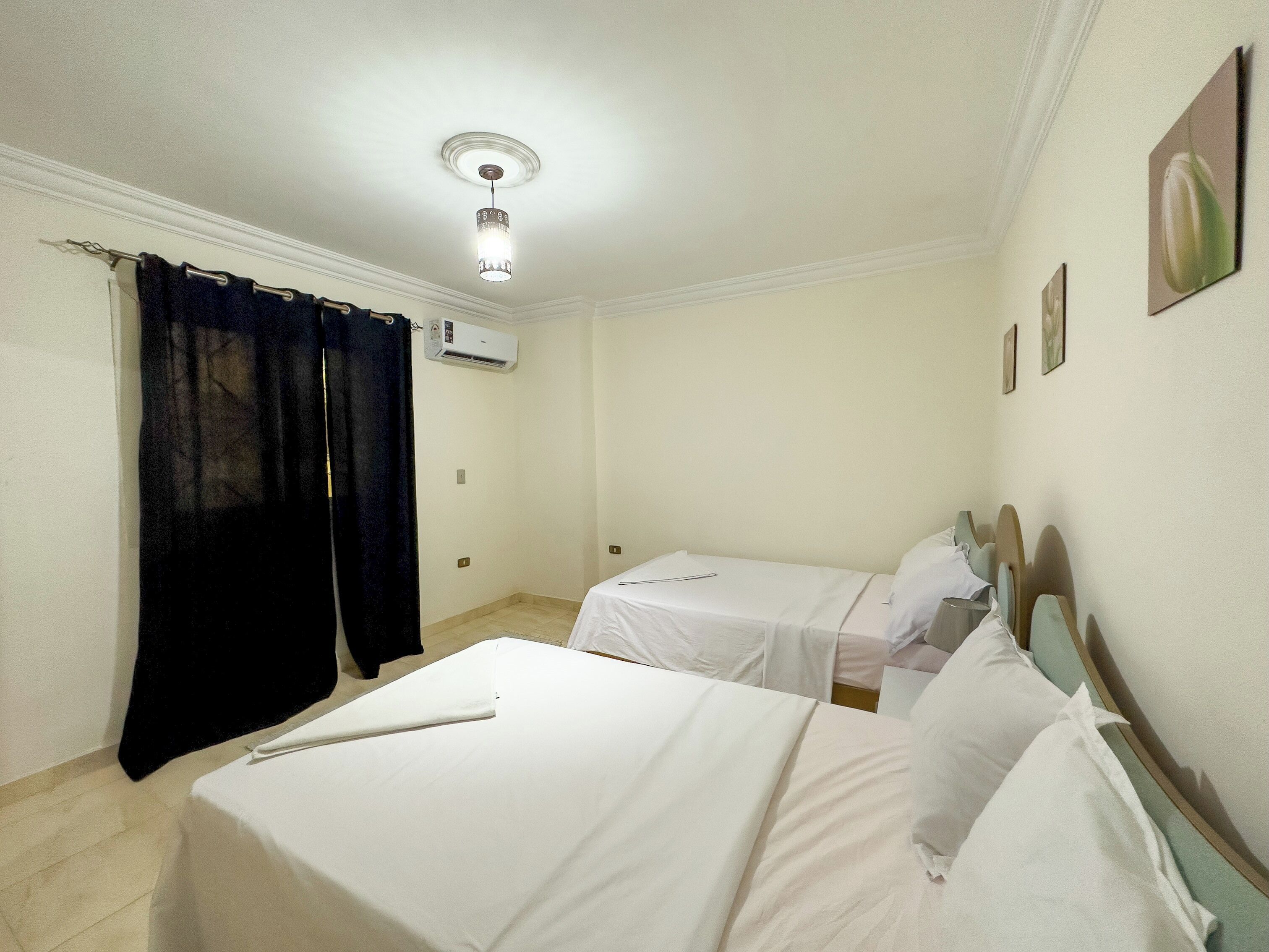 A hotel room with two beds, a curtain, an air conditioning unit, and a ceiling light.