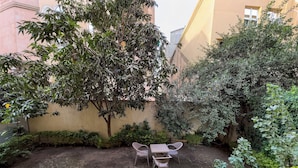 Un patio con una mesa y sillas, rodeado de follaje denso y una pared de edificio.