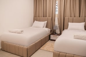 A hotel room with two beds, a nightstand, a lamp, and a window with curtains. - 832 . Modern 1BR Apartment | Near AUC (New Cairo City)