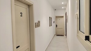 Käytävä, jossa on ovet numeroitu 1 ja 2, vaaleanvärinen lattia ja seinillä kehyksiin asetetut taulut.