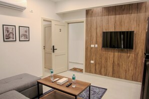 Ein modernes Wohnzimmer mit einer Couch, einem Couchtisch, einem an einer Holzwand montierten Fernseher und einer Tür mit einer Nummer.