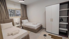Habitació d'hotel amb llit, una tauleta de nit, una làmpada, un armari i una finestra amb cortines.