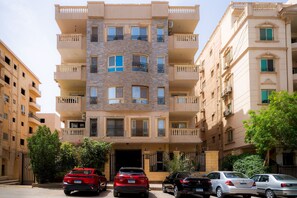 A multi-story residential building with balconies, a gated entrance, and parked cars. - 832 . Modern 1BR Apartment | Near AUC (New Cairo City)