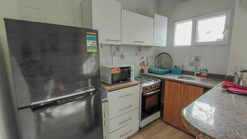 A kitchen with a stainless steel refrigerator, a microwave, a stove, and wooden cabinets.