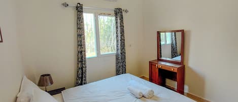 A bedroom with a bed, a bedside table, a mirror, and a window with curtains.